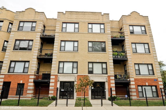 Front view of a multi-story apartment building with balconies and gated entrance.