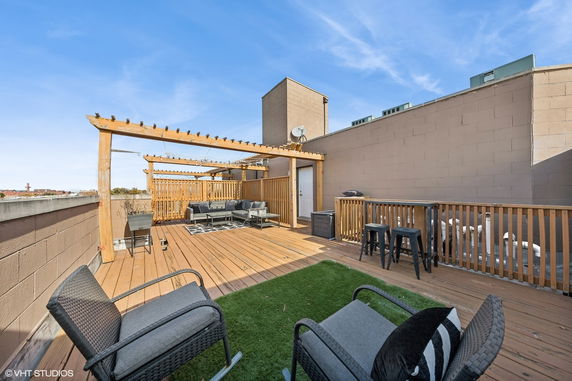 Rooftop area with seating under a wooden pergola, featuring a small artificial lawn and outdoor furniture.