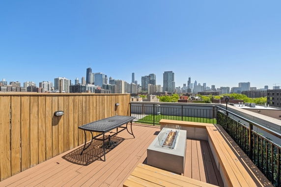 Rooftop deck with a table and bench seating, offering a view of the city skyline.
