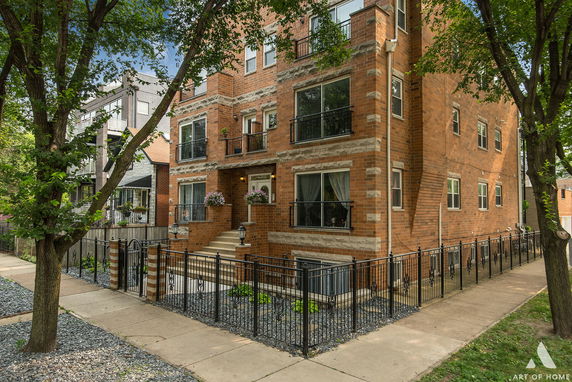 Front view of a multi-story brick building with large windows and a gated entrance.
