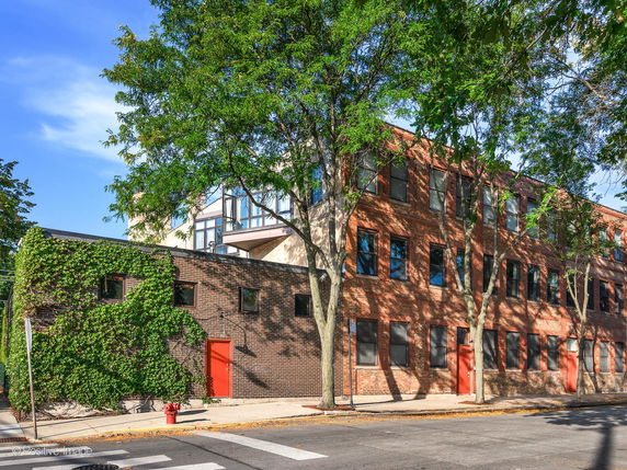 Front view of a multistory brick building with red doors and ivy-covered walls.