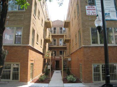 Front view of a multi-story brick building with balconies and an open house sign.