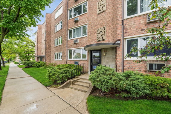 Front view of a brick apartment building with multiple windows and entrance steps.
