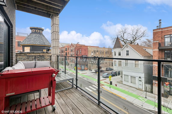 View from an outdoor balcony with seating overlooking a street and neighboring buildings.