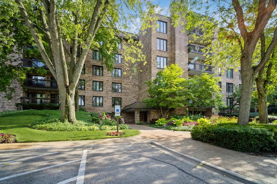 Front view of a multi-story brick apartment building with balconies and surrounding greenery.