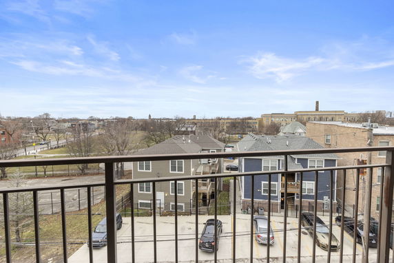 Panoramic view from a balcony overlooking a residential area with parked cars and distant buildings.