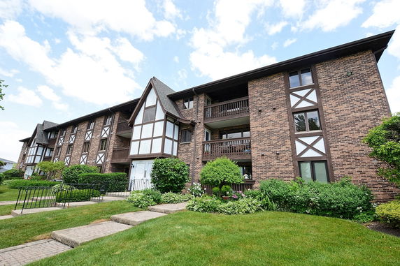 Front view of a multi-story brick building with balconies and a sloped roof.