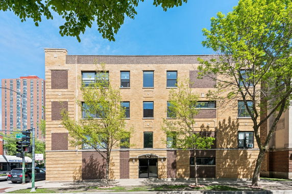 Front view of a multi-story brick building with several windows and trees in front.