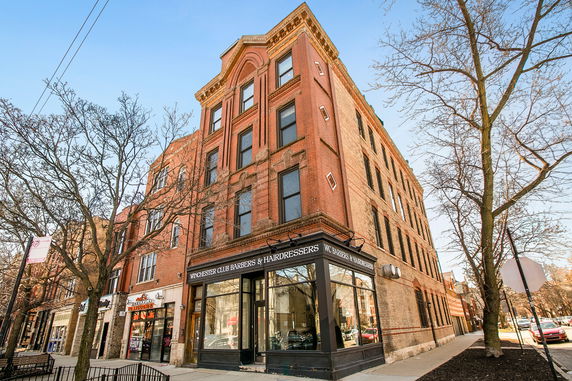 Front view of a multi-story brick building with a barber shop on the ground floor.