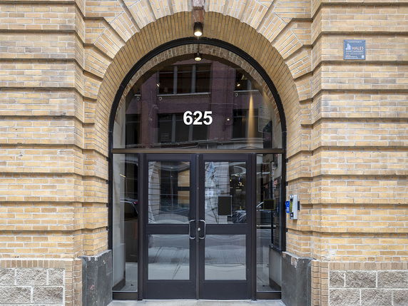 Front view of a building entrance with an arched brick design, glass doors, and the number 625 above the entrance.
