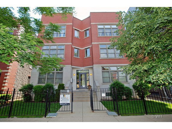 Front view of a multi-story brick building with large windows and a gated entrance.