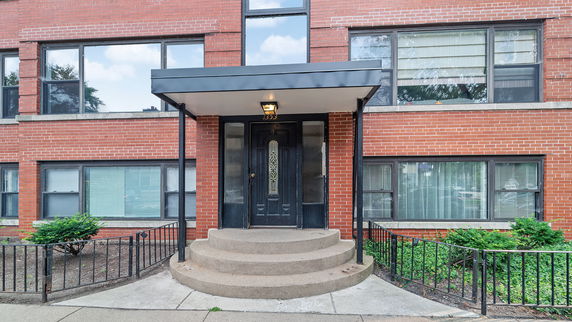 Front view of a brick building entrance with black door and steps.