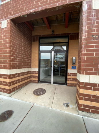 Entrance of a brick building with glass doors and an overhead shelter.