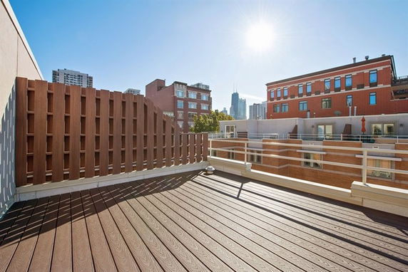 Rooftop view with a wooden deck and low railing, surrounded by urban buildings in the background.