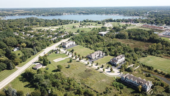 Aerial view of residential area with houses, roads, and green spaces near a body of water.