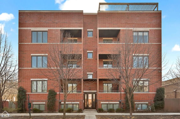 Front view of a brick apartment building with multiple balconies and large windows.
