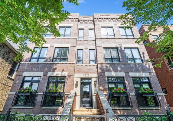 Front view of a multi-story brick apartment building with large windows and a central entrance.