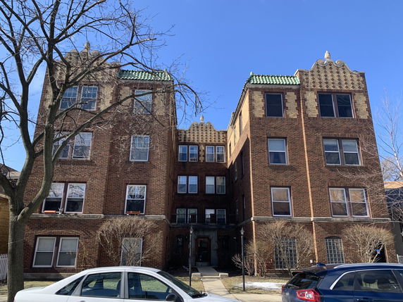 Front view of a multi-story brick apartment building with decorative roof elements.