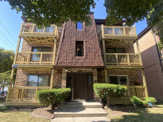 Front view of a three-story apartment building with wooden balconies and a central entrance.