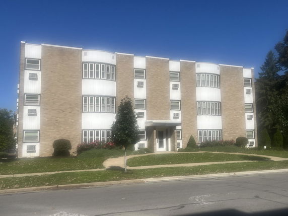 Front view of a multi-story apartment building with a brick facade and multiple windows.
