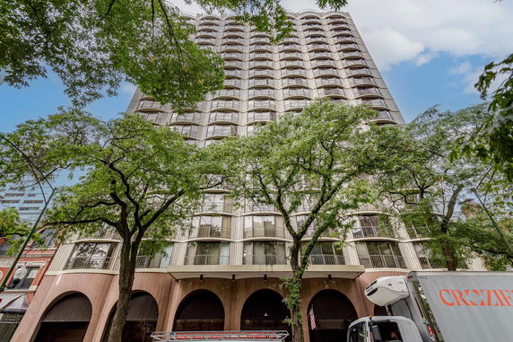 Front view of a high-rise building with many windows and a series of arches at the base.