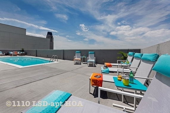 Rooftop area with a swimming pool and lounge chairs, featuring a sunny sky in the background.