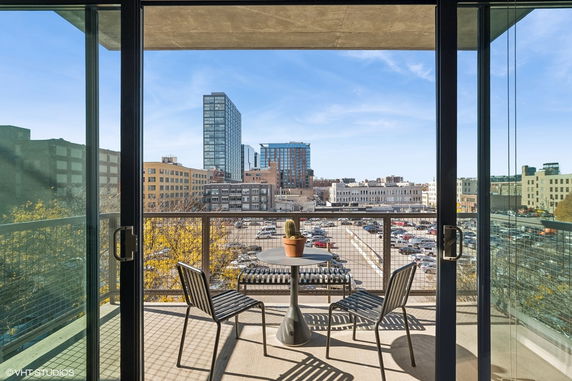 Panoramic view of city buildings seen from a balcony with chairs and table.