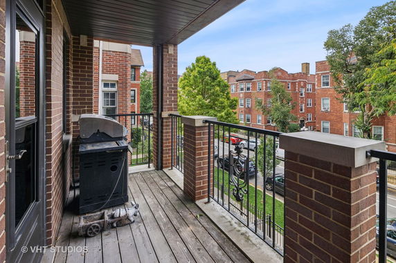 View from a brick balcony overlooking nearby residential buildings and a tree-lined street.