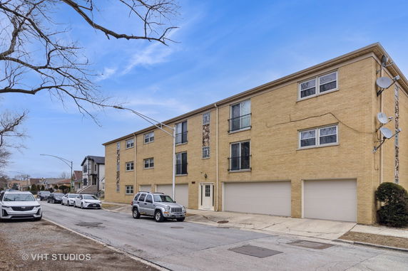 Front view of a three-story brick apartment building with garages at the ground level.