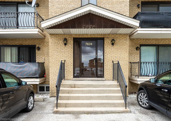 Front view of a brick apartment building entrance with steps leading to a glass door.