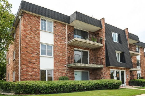 Front view of a three-story brick apartment building with balconies.