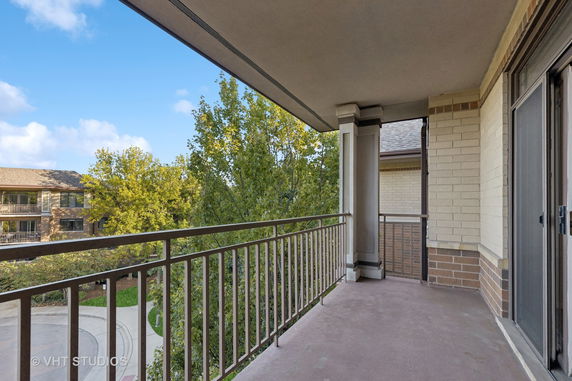 View from a balcony overlooking trees and a neighboring building.