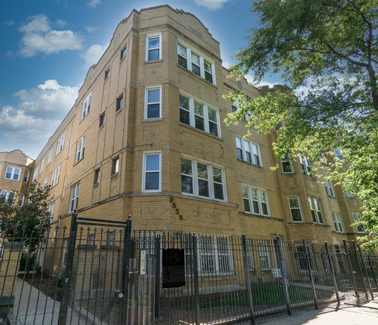 Front view of a multi-story apartment building with yellow brick facade and several windows.