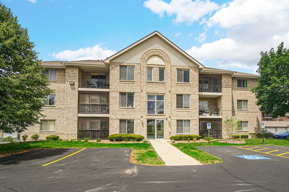 Front view of a three-story apartment building with a gable roof and multiple balconies.
