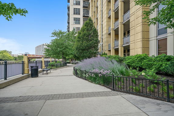 Pathway along a residential building with greenery and benches.