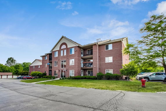 Front view of a three-story brick apartment building with parking area.