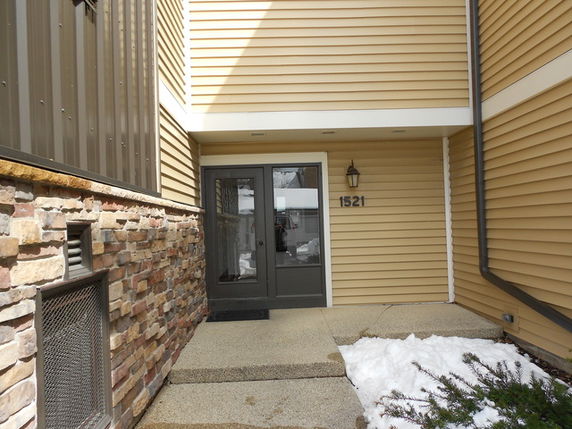 Front view of a house with beige siding and stone accent wall, featuring double glass doors.