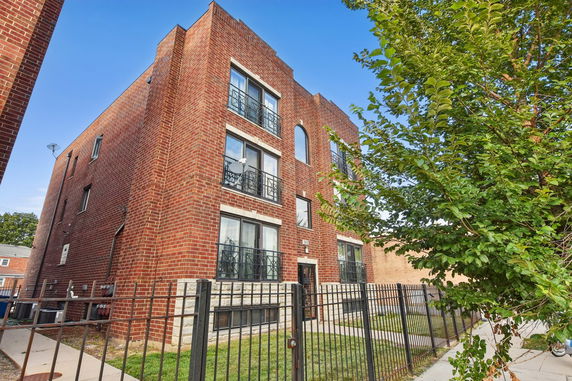 Front view of a multi-story brick building with metal railings and a fenced yard.