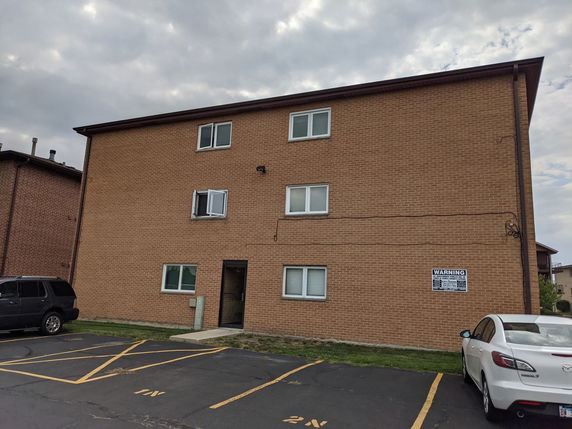 Front view of a three-story brick building with several windows and parked cars in front.
