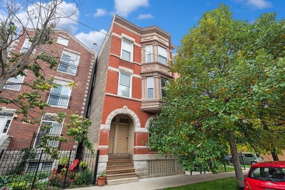 Front view of a three-story brick building with arched entrance and bay windows.