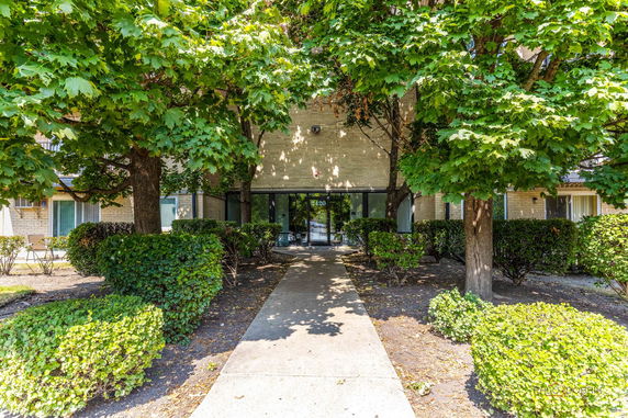Front view of a building entrance with trees and bushes.