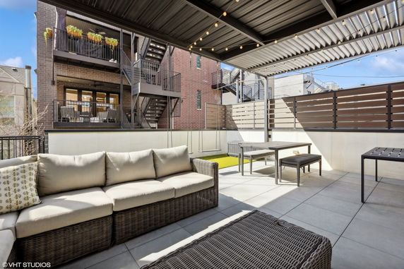 Rooftop area with seating and dining table, surrounded by buildings.