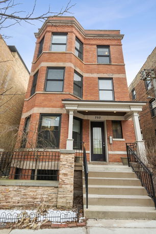 Front view of a three-story brick townhouse with a small porch and black railings.
