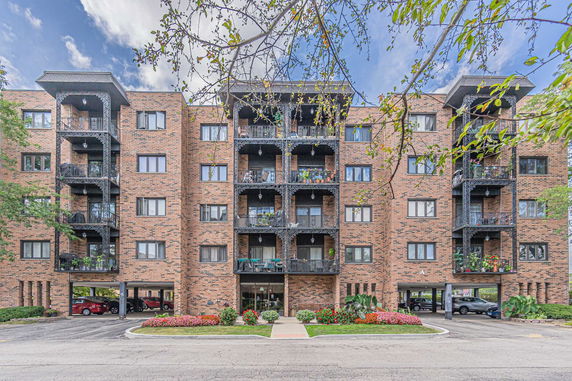 Front view of a multi-story brick apartment building with balconies and covered parking area.