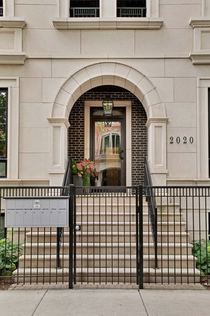 Front view of a building entrance with steps, black railings, and an arched doorway.