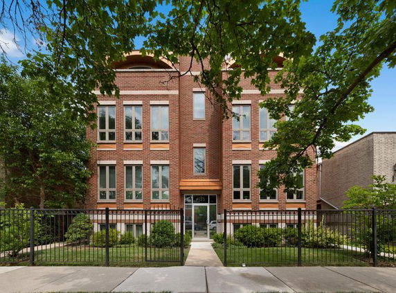 Front view of a multi-story brick building with large windows and a gated entrance.