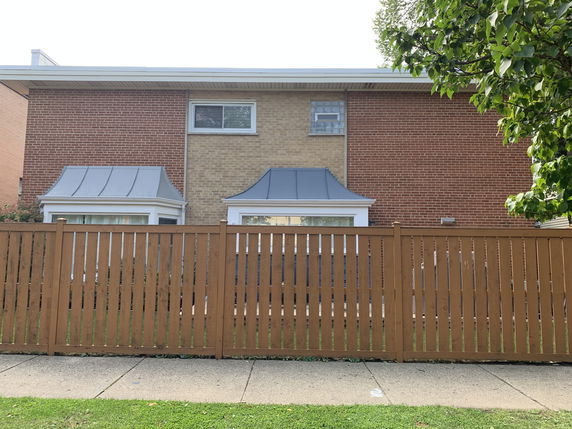 Front view of a two-story house with a brick exterior and a wooden fence.