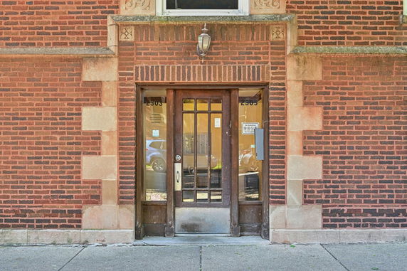Front view of a brick building entrance with a glass door and decorative stonework.