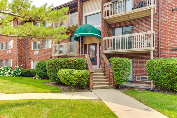 Front view of a multi-story brick apartment building with balconies and greenery.