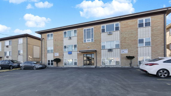 Front view of a three-story apartment building with a brick exterior and a central entrance.